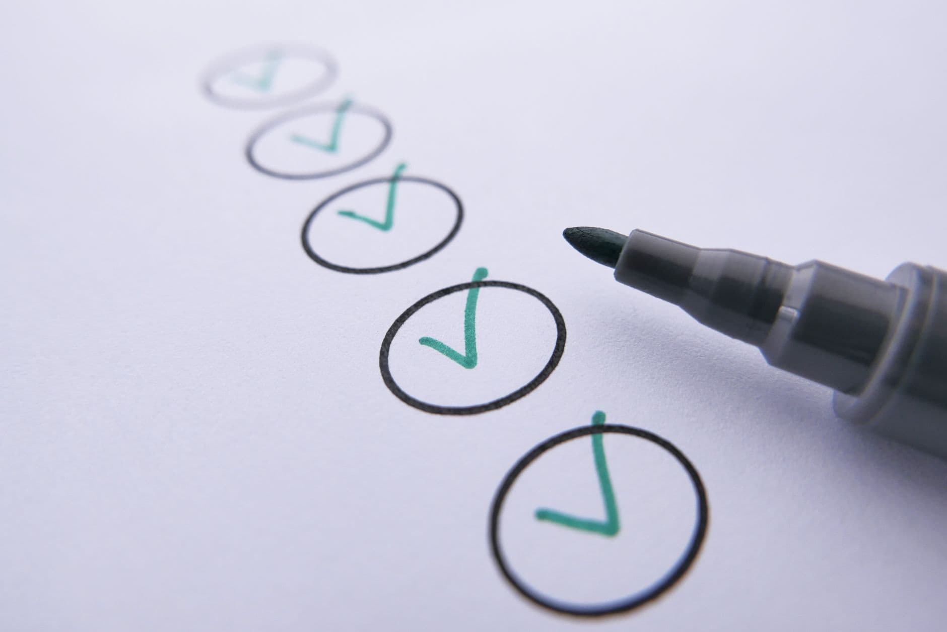 Close-up of a checklist with green checkmarks on white paper using a marker.